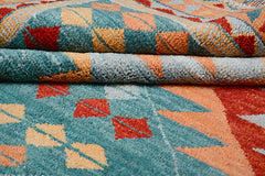A handmade Afghan wool rug featuring a geometric pattern in teal, orange, and red.