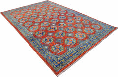 A handmade Afghan wool rug featuring a repeating geometric pattern in orange, blue, and green.