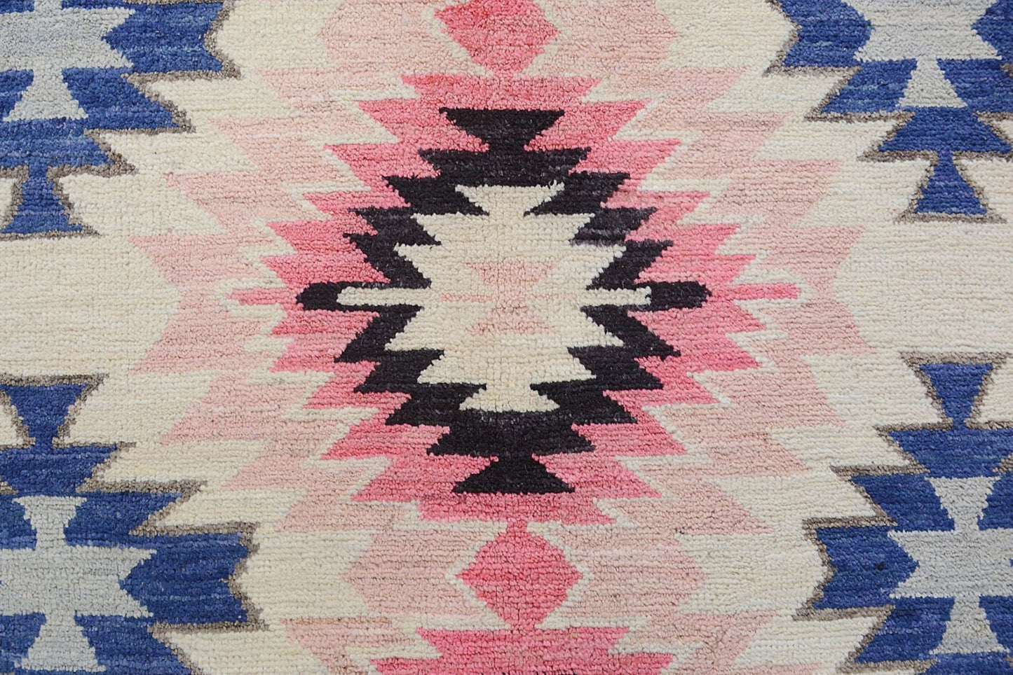 Handmade Afghan wool rug featuring a geometric tribal pattern in pink, black, blue, and cream.