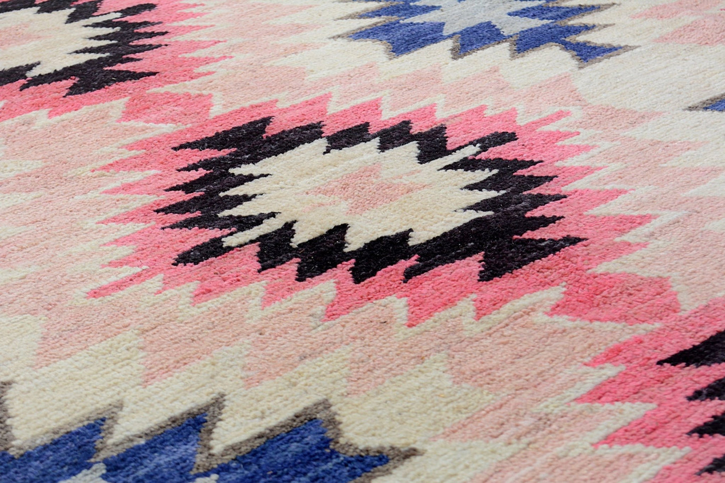 A handmade Afghan wool rug featuring a geometric tribal pattern in pink, blue, and cream tones.