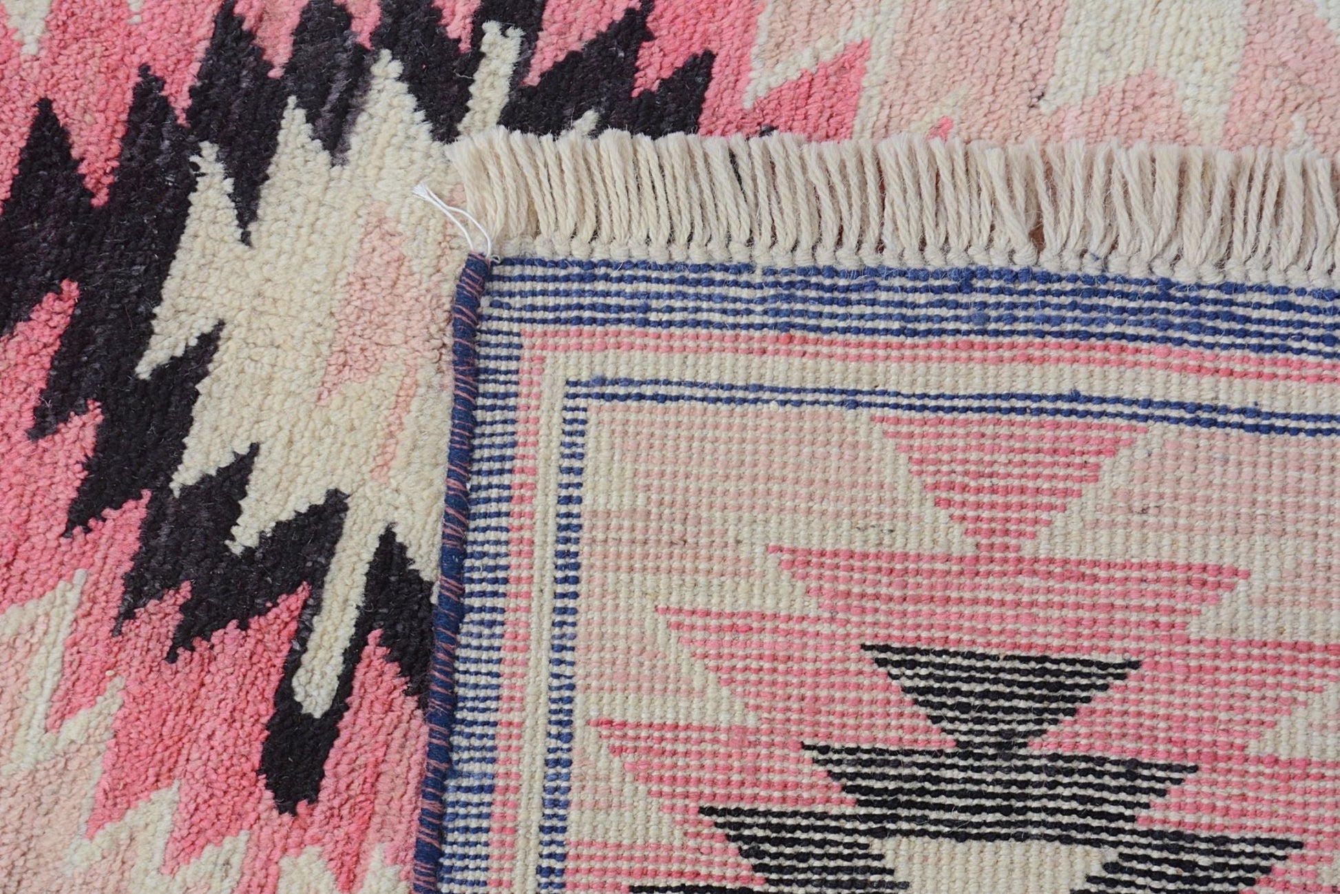 A close-up of a handmade Afghan wool rug featuring a geometric pattern in pink, black, and cream.