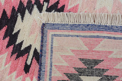 A close-up of a handmade Afghan wool rug featuring a geometric pattern in pink, black, and cream.