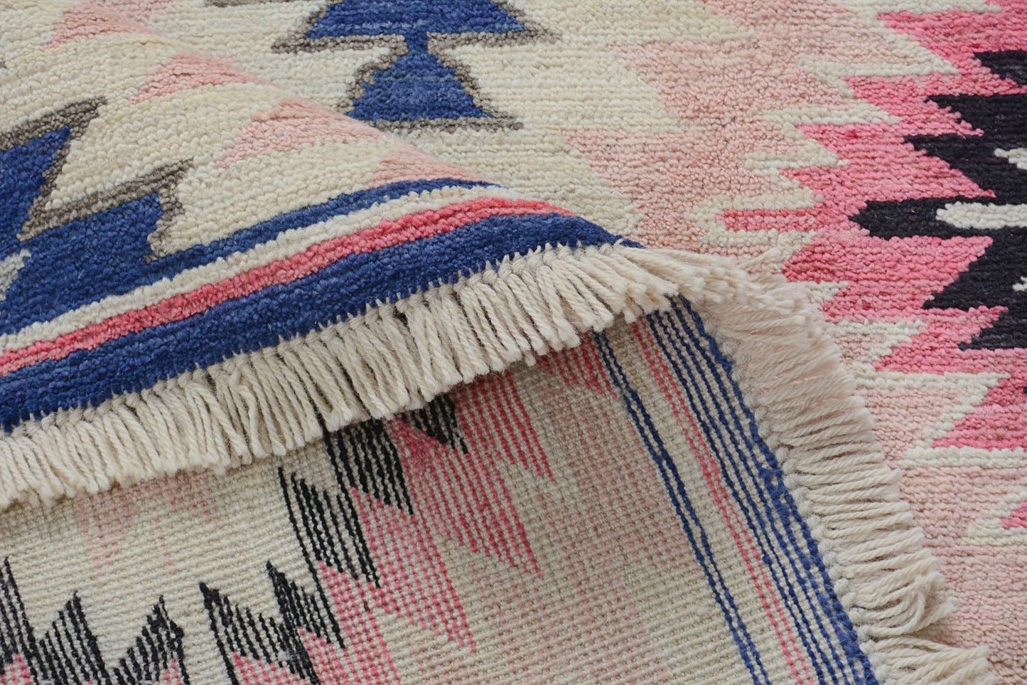 A handmade Afghan wool rug featuring a geometric tribal pattern in pink, blue, and black.