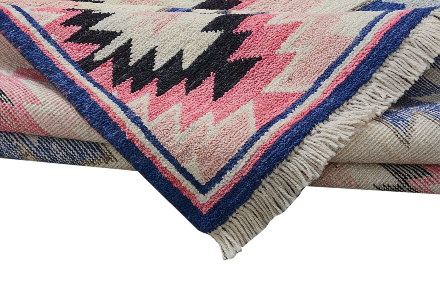 A folded Afghan Pashm wool rug featuring a geometric tribal pattern in pink, black, and blue.