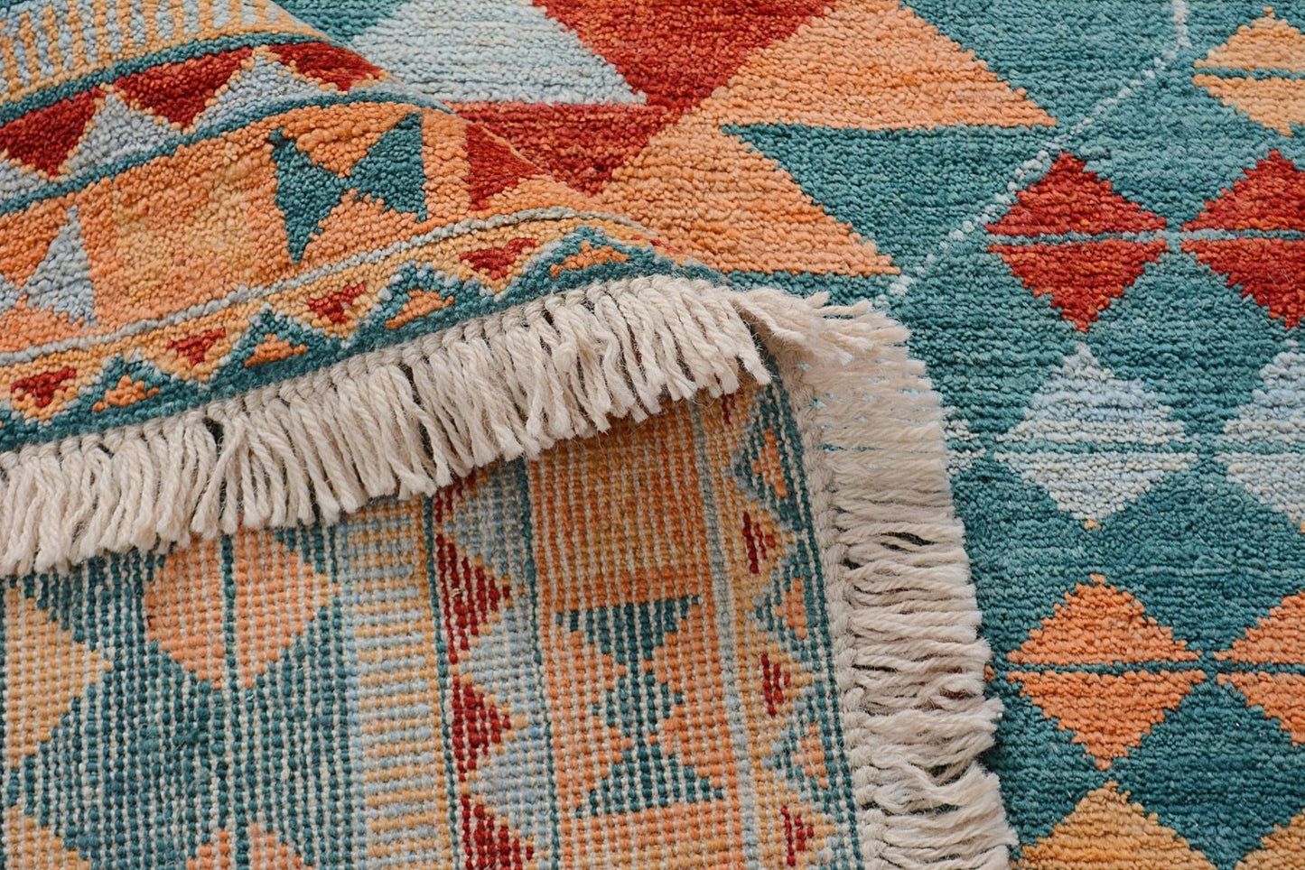 A handmade Afghan wool rug featuring a geometric pattern in teal, orange, and red with fringe.