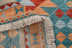 A handmade Afghan wool rug featuring a geometric pattern in teal, orange, and red with fringe.