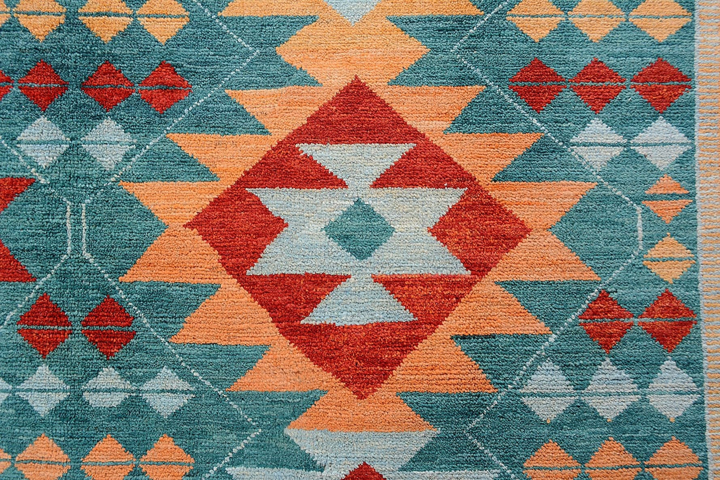 A handmade Afghan wool rug featuring a geometric tribal pattern in teal, orange, and red.