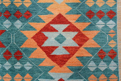 A handmade Afghan wool rug featuring a geometric tribal pattern in teal, orange, and red.