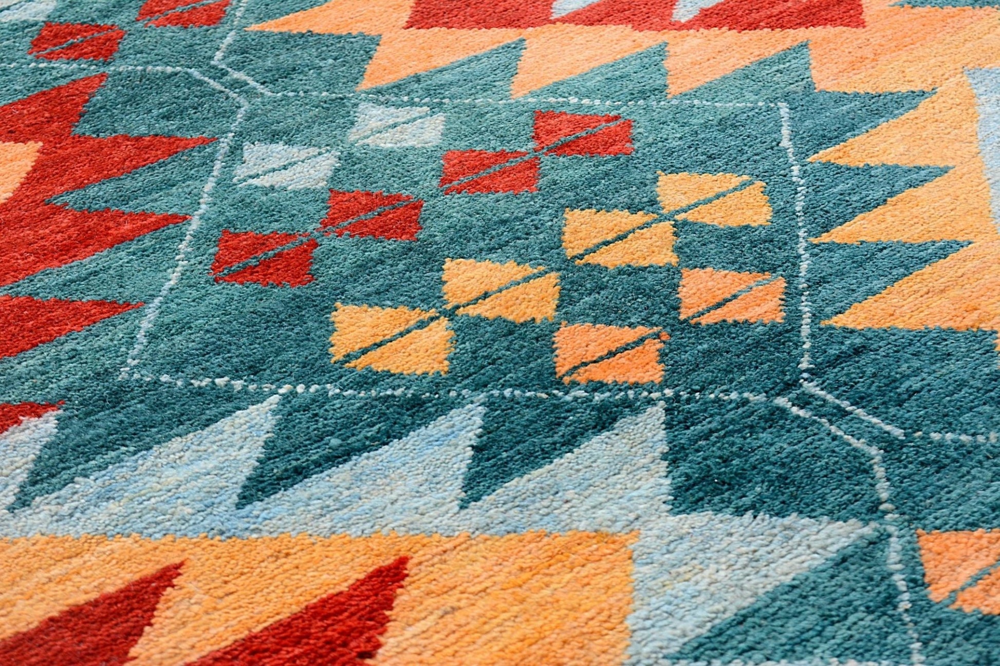 A handmade Afghan wool rug featuring a geometric tribal pattern in teal, red, and orange.