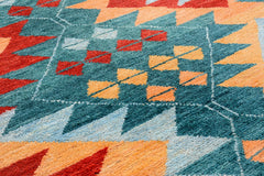 A handmade Afghan wool rug featuring a geometric tribal pattern in teal, red, and orange.
