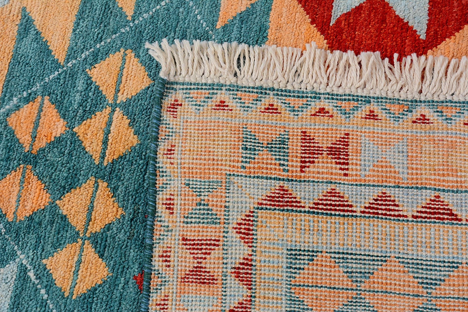 A close-up of a handmade Afghan wool rug featuring geometric patterns in teal, orange, and red.