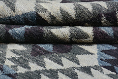 A close-up of a handmade Afghan wool rug featuring a geometric pattern in grey, blue, and cream.