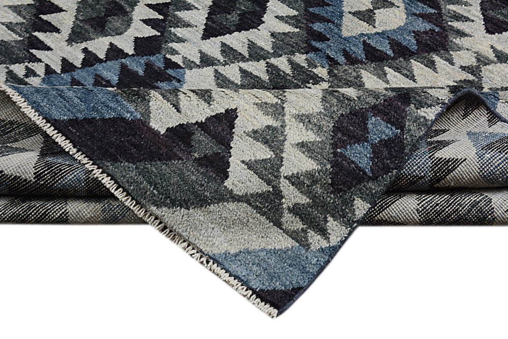 A handmade Afghan wool rug featuring a geometric pattern in shades of blue, grey, and black.