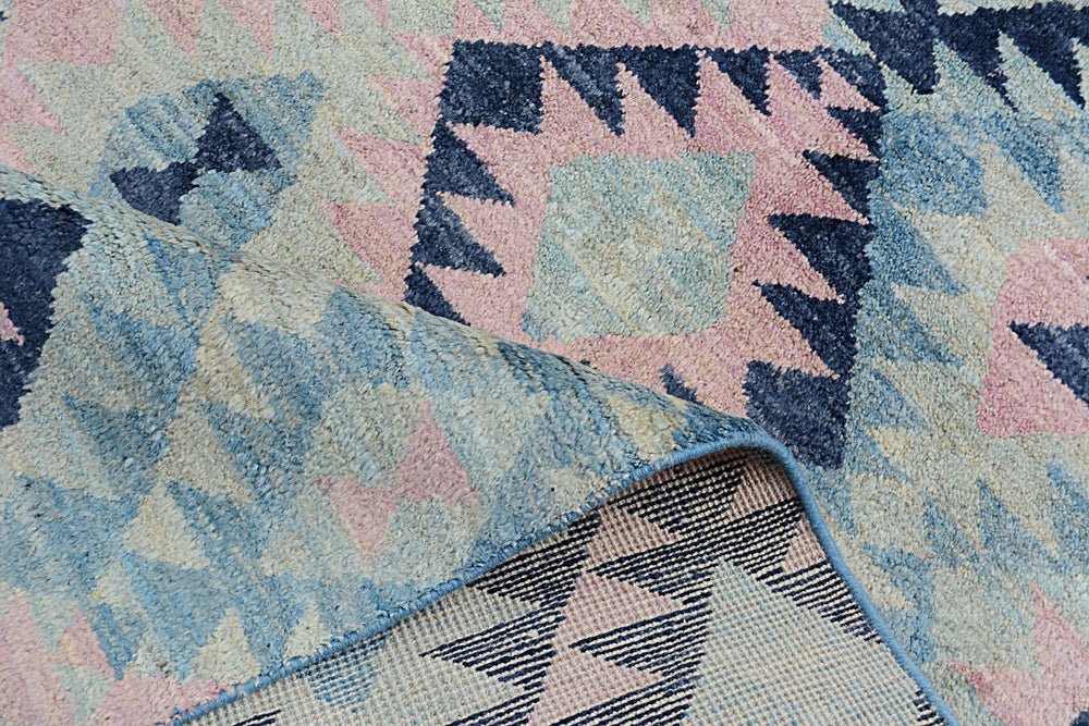 A handmade Afghan wool rug featuring a geometric pattern in shades of blue, pink, and cream.