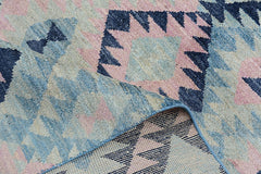A handmade Afghan wool rug featuring a geometric pattern in shades of blue, pink, and cream.