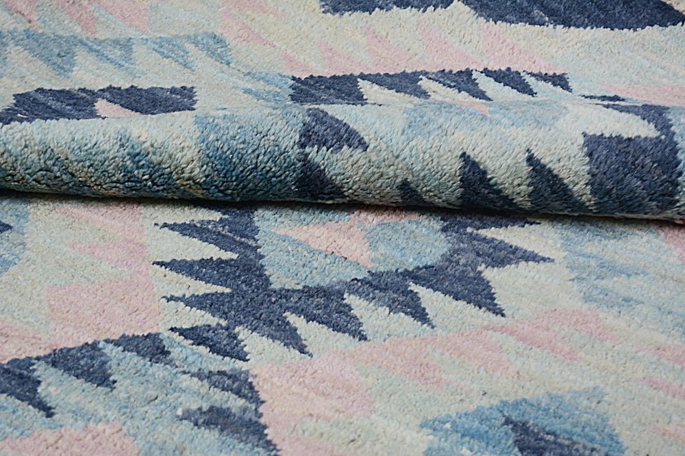 A handmade Afghan wool rug featuring a geometric pattern in shades of blue, pink, and cream.