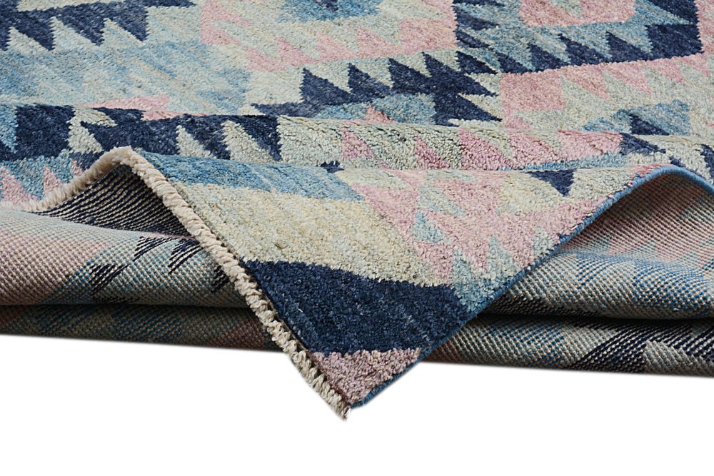 A handmade Afghan wool rug featuring a geometric pattern in shades of blue, pink, and cream.