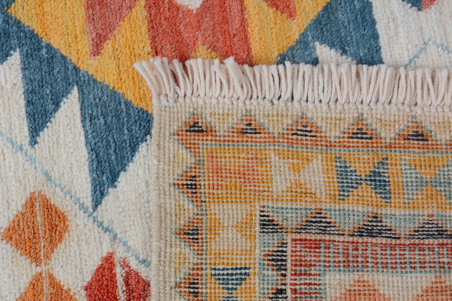A close-up of a handmade Afghan wool rug featuring a geometric pattern with a fringed edge.