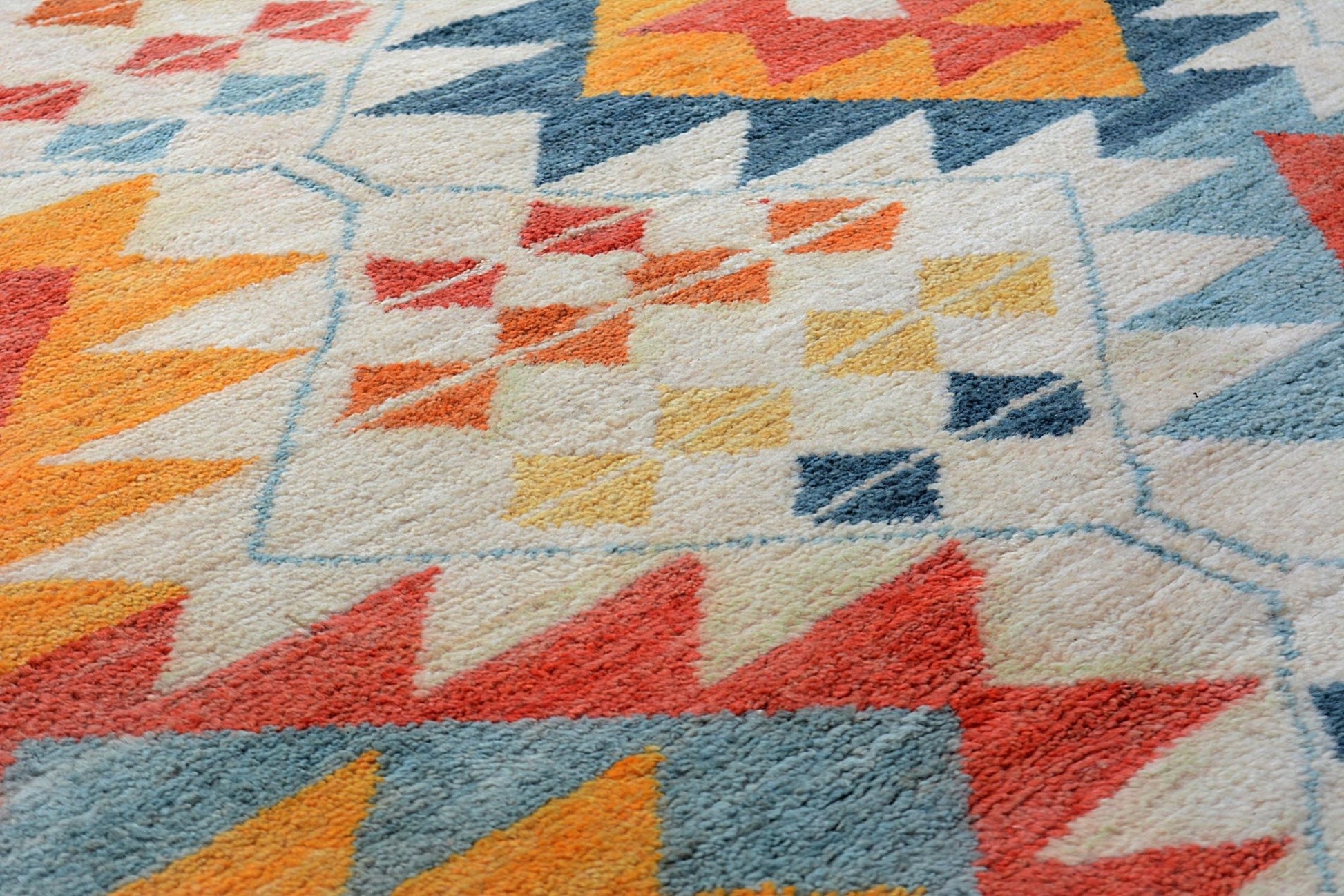 A handmade Afghan wool rug featuring a geometric tribal pattern in orange, blue, and cream.