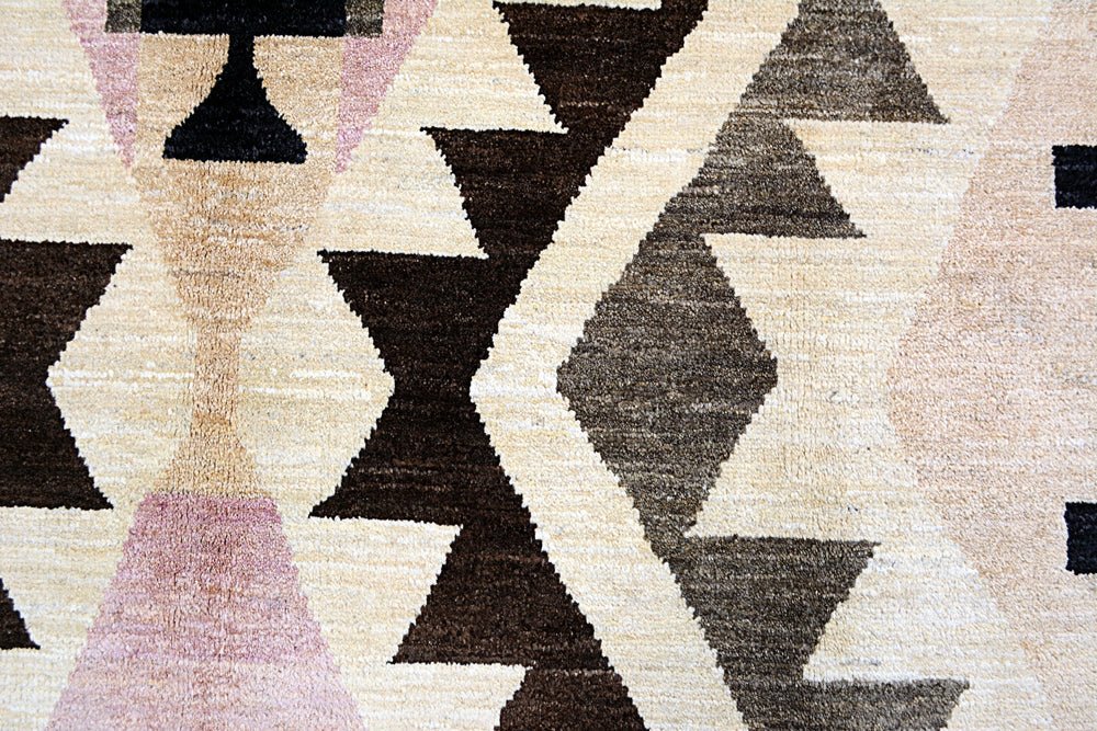 A handmade Afghan wool rug featuring a geometric pattern in shades of brown, cream, and soft pink.