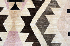 A handmade Afghan wool rug featuring a geometric pattern in shades of brown, cream, and soft pink.