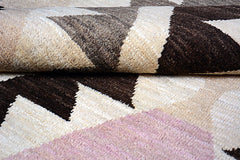 A handmade Afghan wool rug featuring a geometric pattern in shades of brown, cream, and pink.