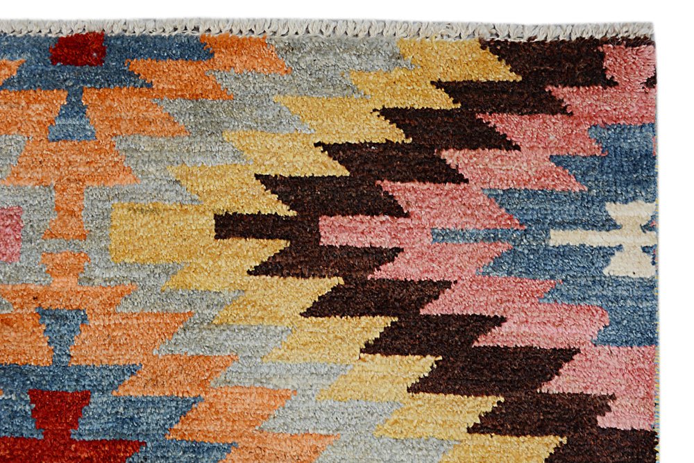 A handmade Afghan wool rug featuring a colorful geometric kilim pattern in a plush pile.