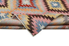 Handmade Afghan wool rug featuring a colorful geometric kilim pattern with a folded corner.