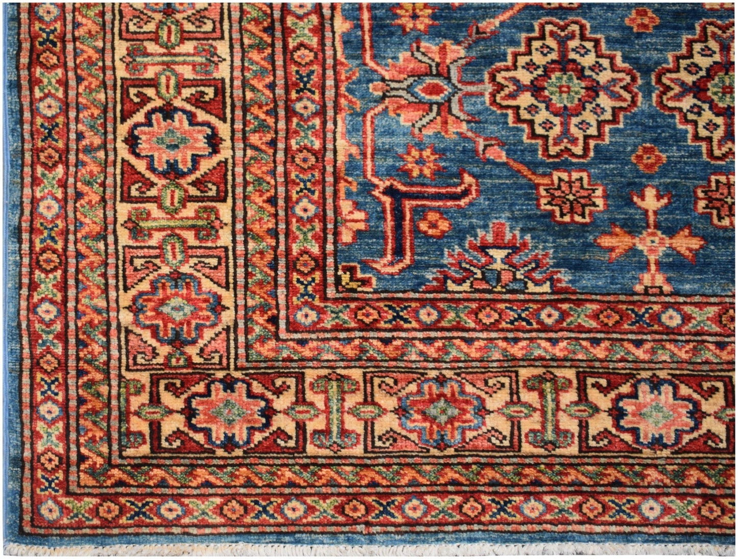 A handmade Afghan Super Kazakh rug featuring a blue field with geometric patterns and red borders.