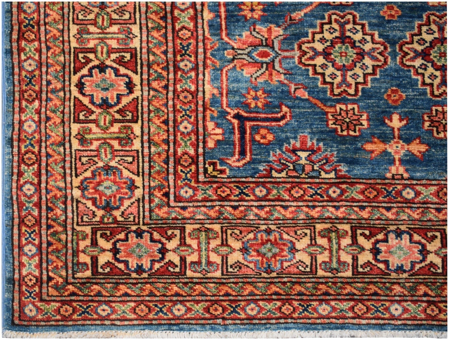A handmade Afghan Super Kazakh rug featuring a blue field with geometric patterns and red borders.