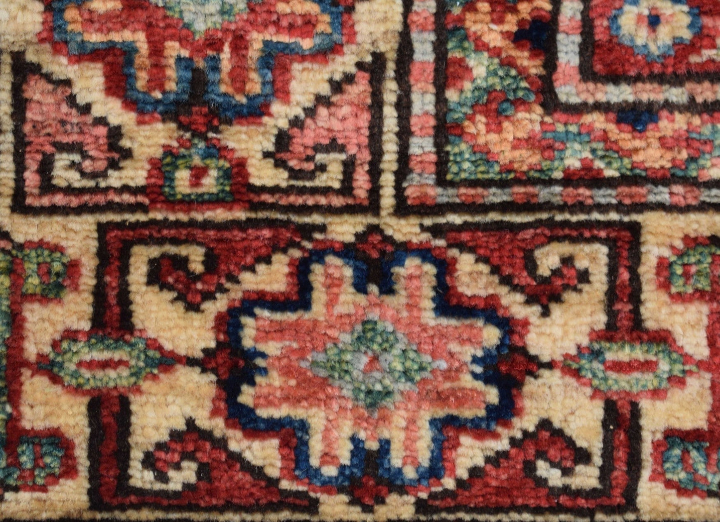 A close-up of an Afghan Super Kazakh rug featuring geometric floral motifs in red, blue, and cream.