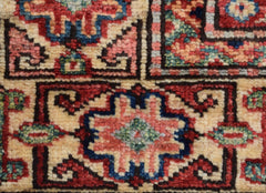 A close-up of an Afghan Super Kazakh rug featuring geometric floral motifs in red, blue, and cream.