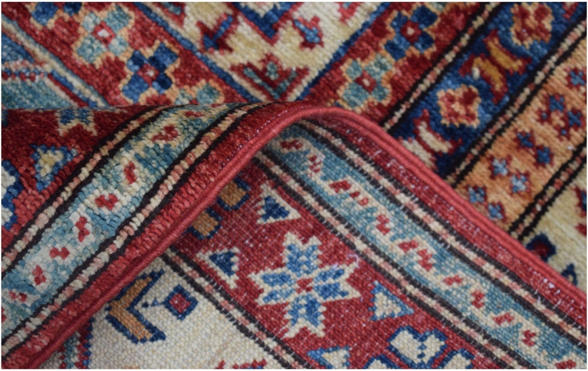 A close-up of a handmade Afghan Super Kazakh rug featuring intricate geometric patterns in red and blue.