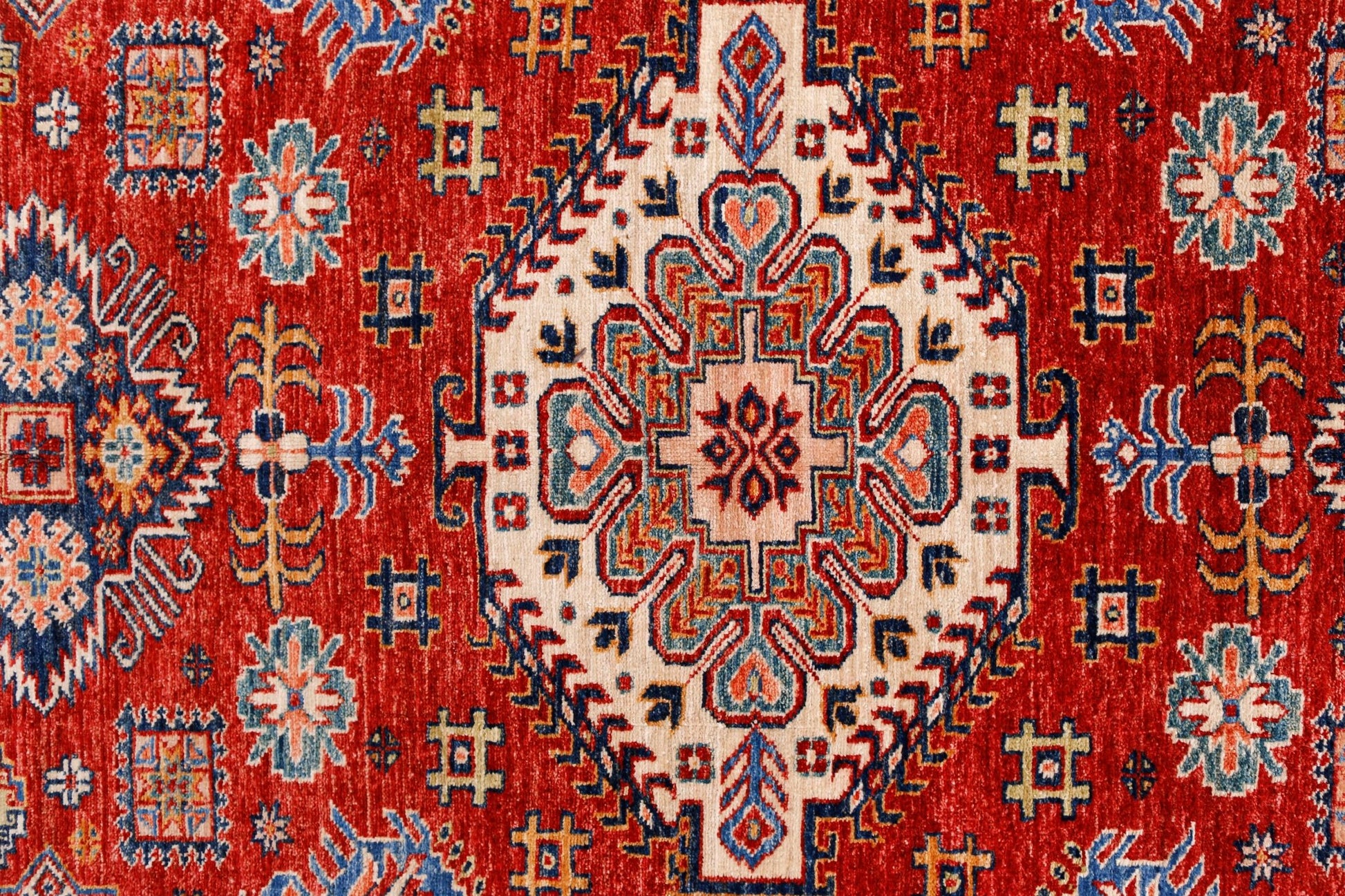 A handmade Afghan Super Kazakh rug featuring a central geometric medallion on a red background.