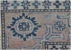A close-up of an Afghan Super Kazakh rug featuring geometric blue and cream patterns on a pink base.