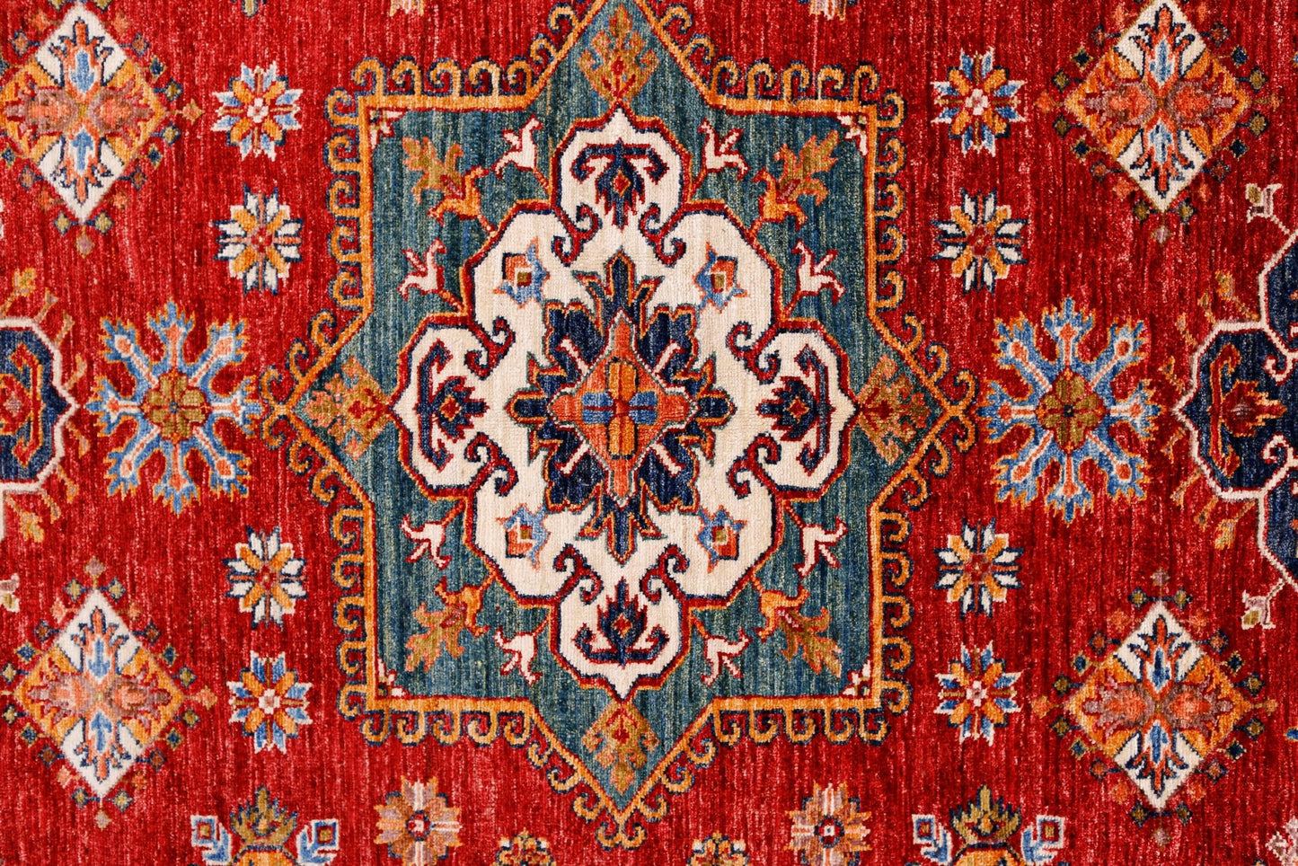 A handmade Afghan Super Kazakh rug featuring a central medallion on a vibrant red field.