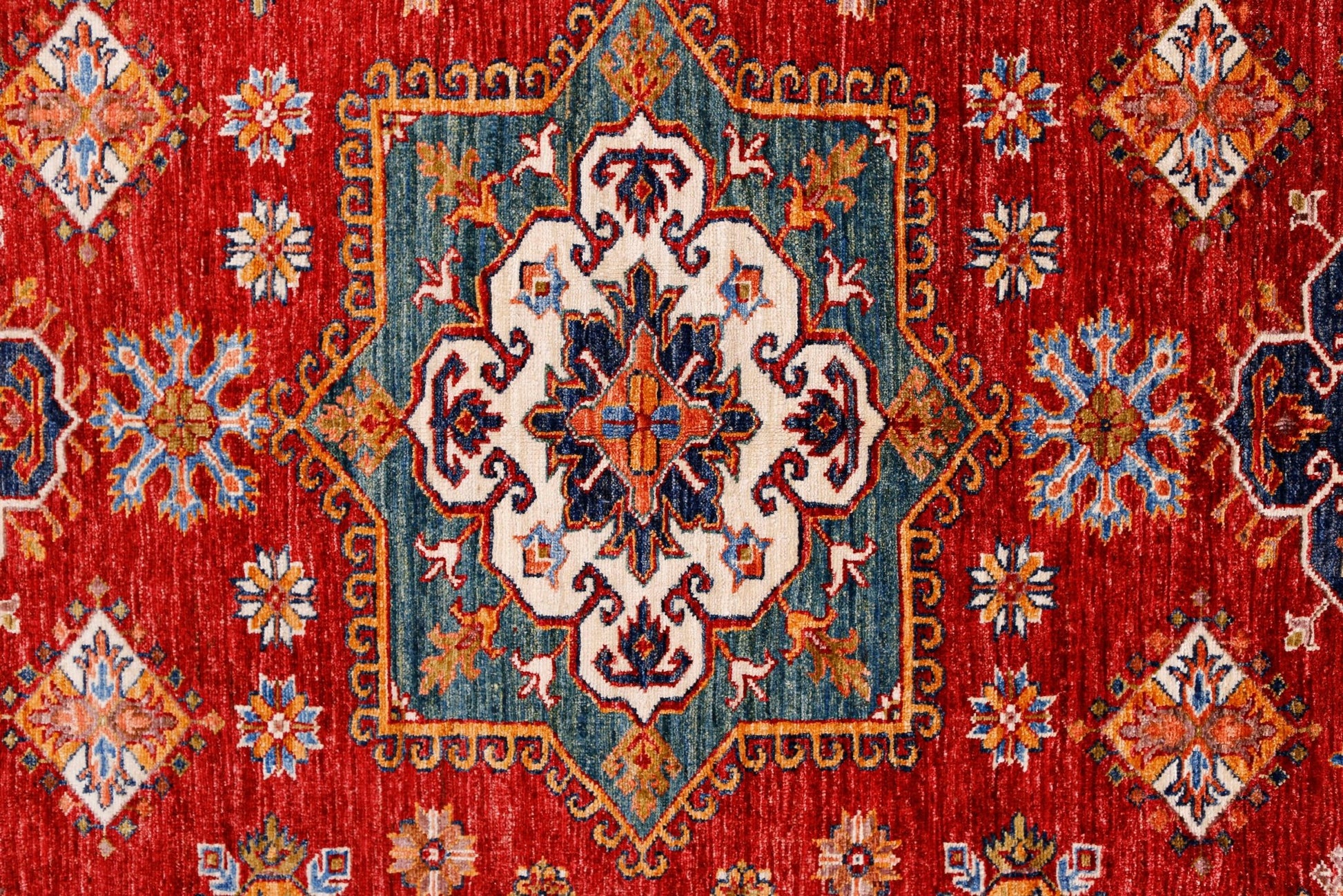 A handmade Afghan Super Kazakh rug featuring a central medallion on a vibrant red field.