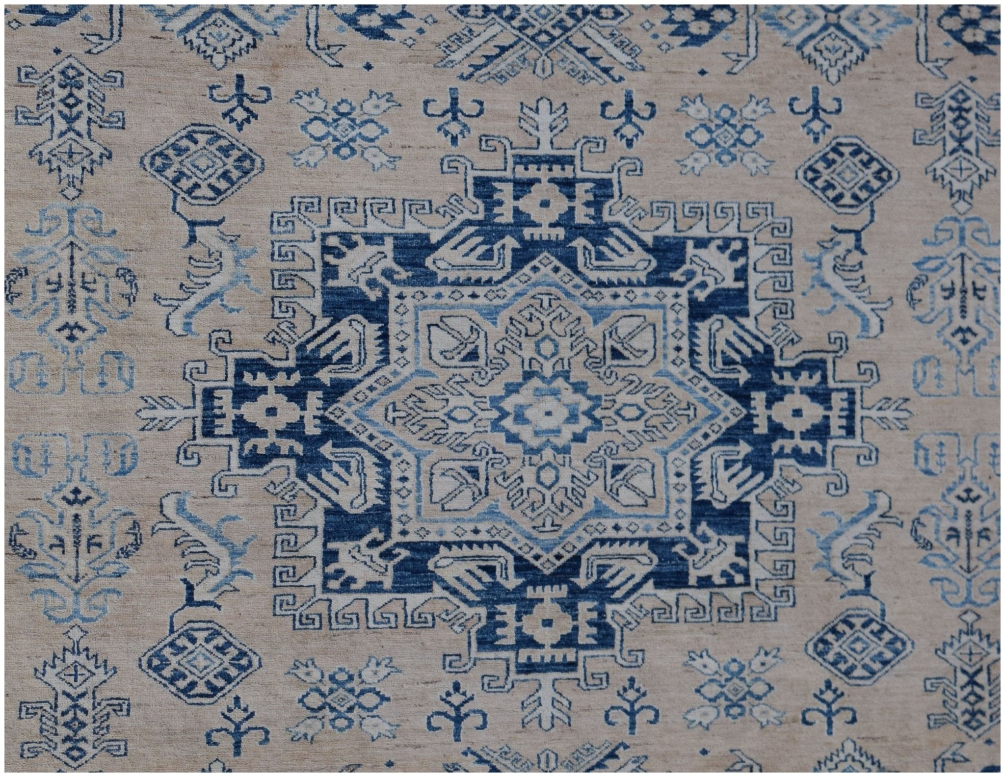 A handmade Afghan Super Kazakh rug featuring a central blue geometric medallion on a beige field.