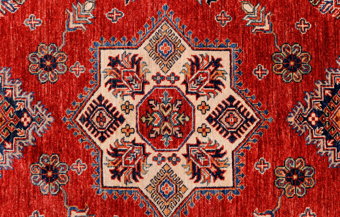 A handmade Afghan Super Kazakh rug featuring a central geometric star motif on a red background.