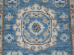 An Afghan Super Kazakh runner rug featuring a blue field with traditional cream floral motifs.