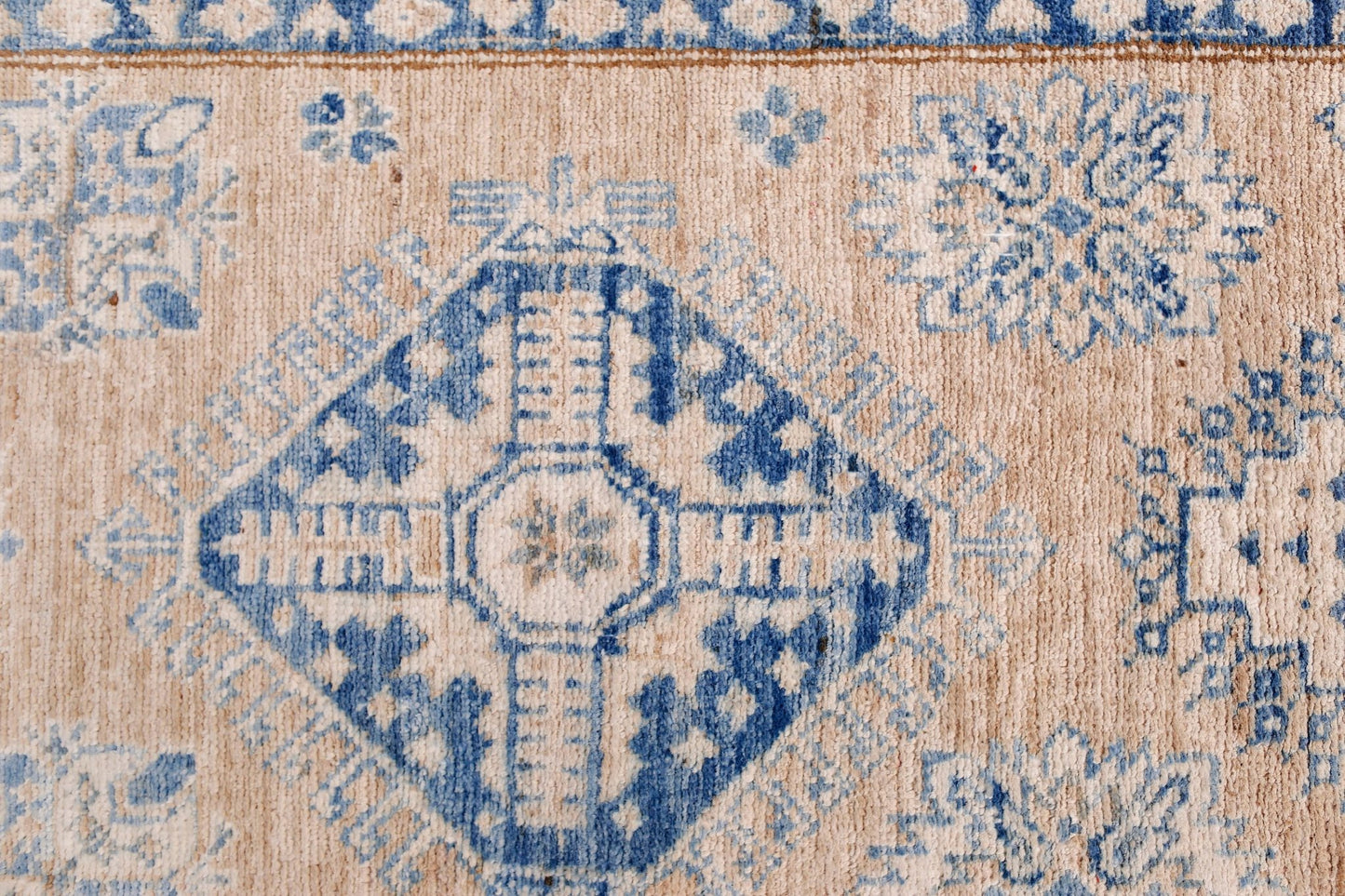 A handmade Afghan Super Kazakh runner featuring traditional blue geometric motifs on a beige wool.
