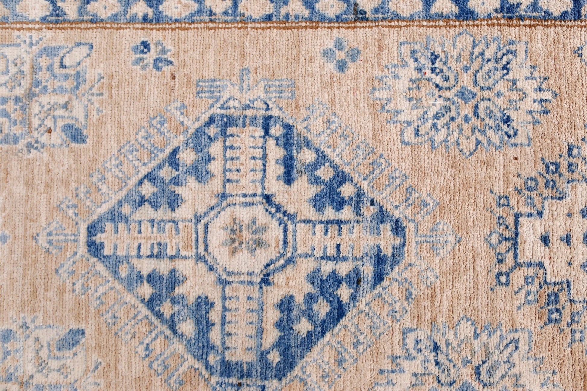 A handmade Afghan Super Kazakh runner featuring traditional blue geometric motifs on a beige wool.