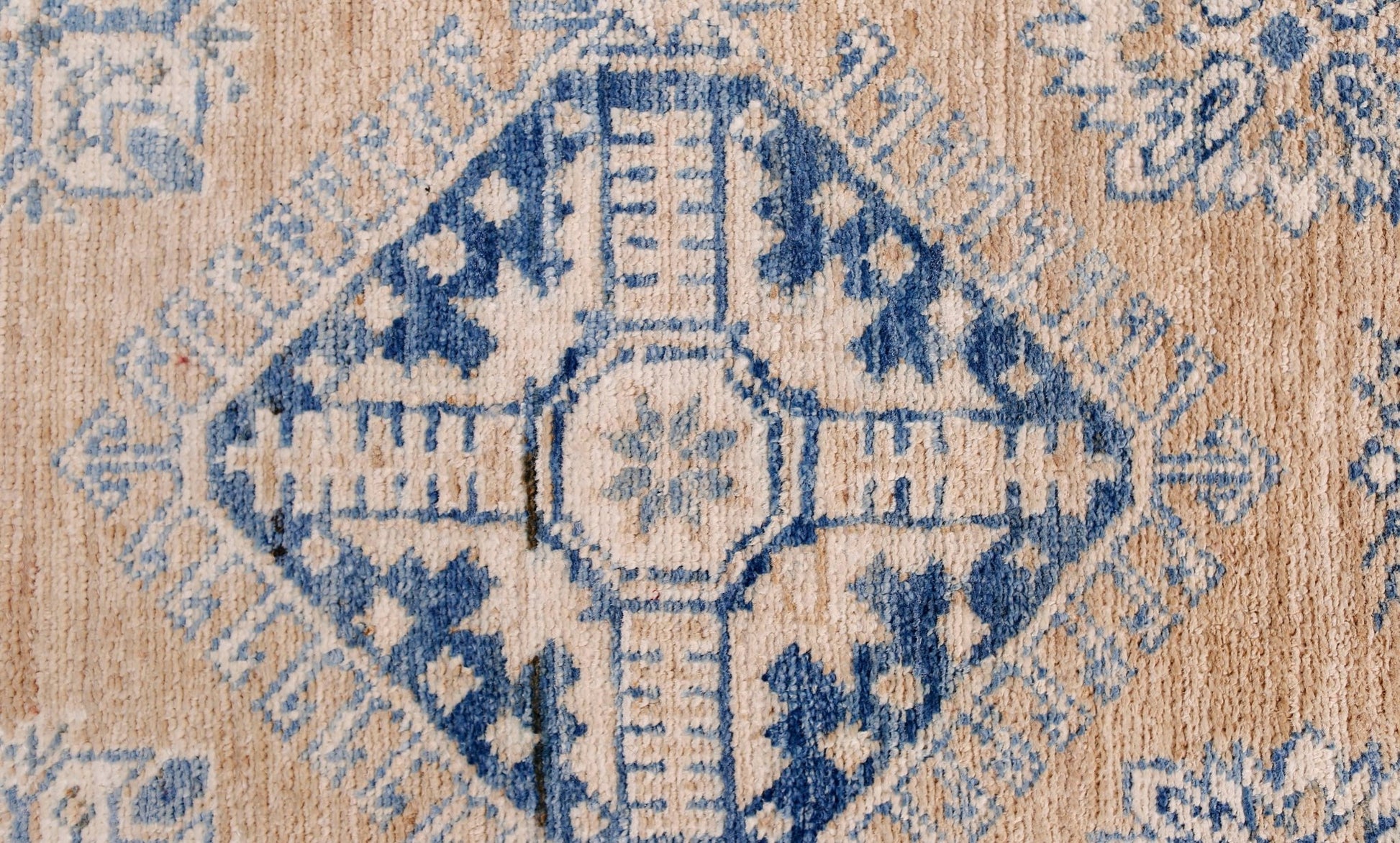 A handmade Afghan Super Kazakh runner featuring a blue geometric diamond pattern on a tan wool base.