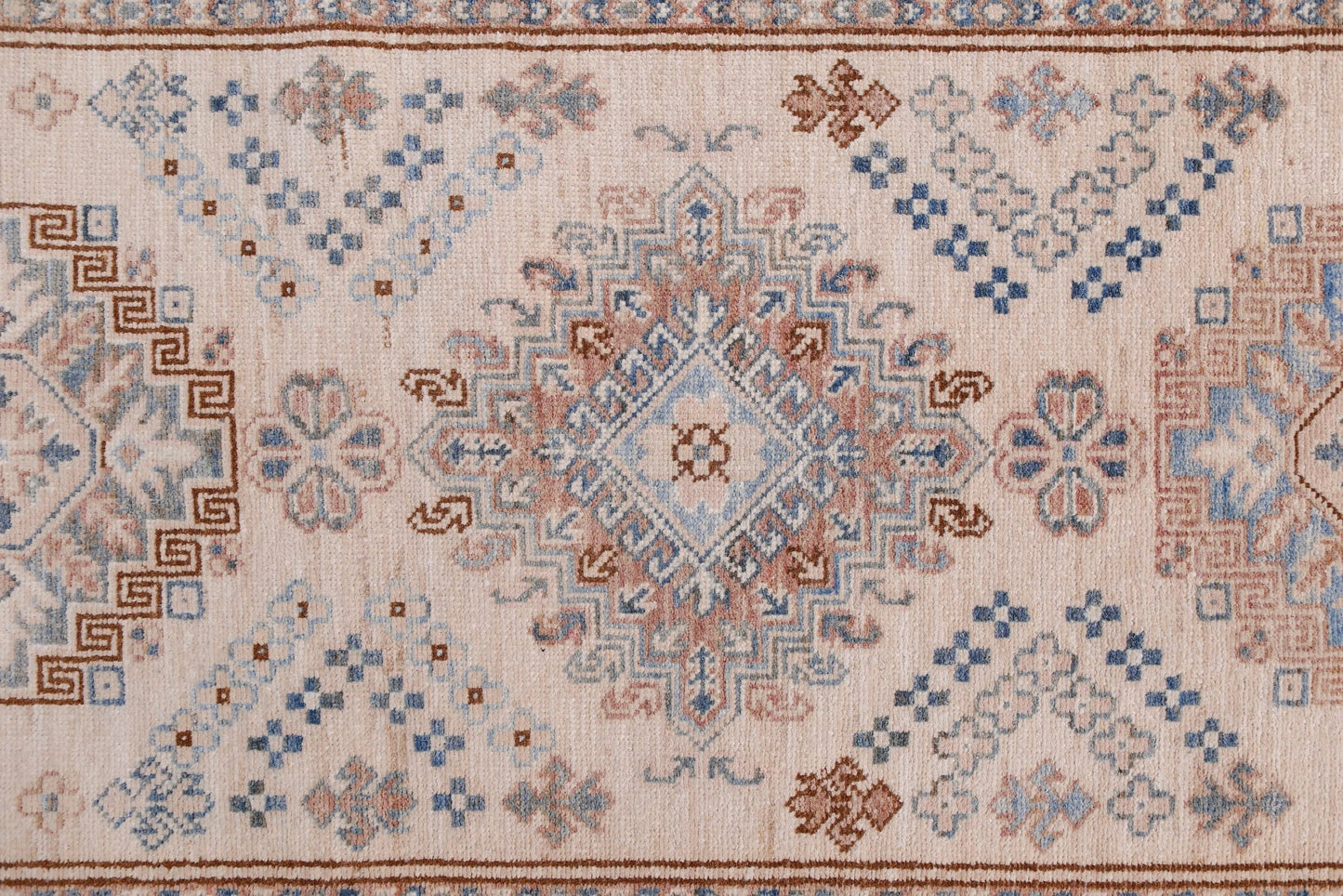 An Afghan Super Kazakh runner featuring traditional geometric motifs in blue and brown on a cream base.