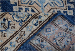 A folded Afghan Super Kazakh runner rug featuring a geometric pattern in blue, beige, and grey.