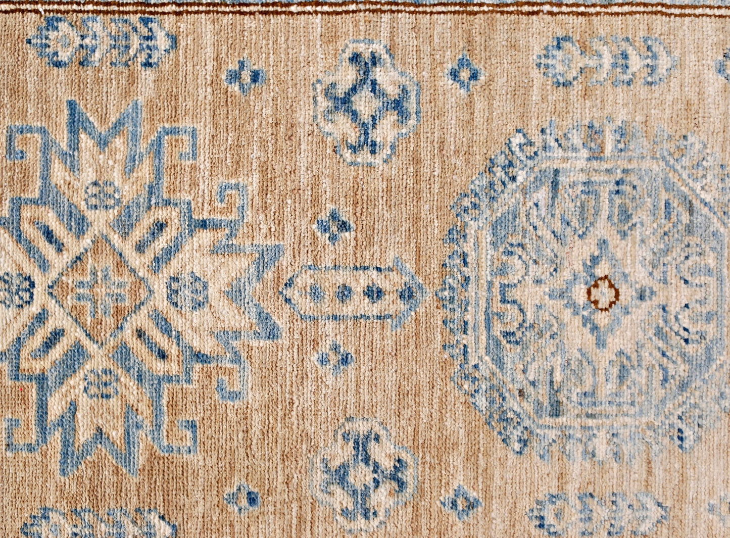 A handmade Afghan Super Kazakh runner featuring traditional blue geometric motifs on a tan wool base.