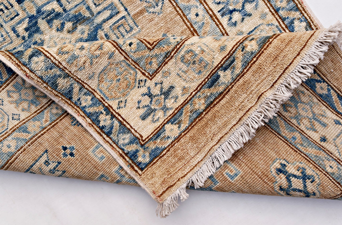 A handmade Afghan Super Kazakh runner featuring traditional blue motifs on a tan wool background.