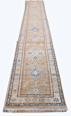 A long, handmade Afghan Super Kazakh runner rug featuring traditional blue geometric motifs on tan.