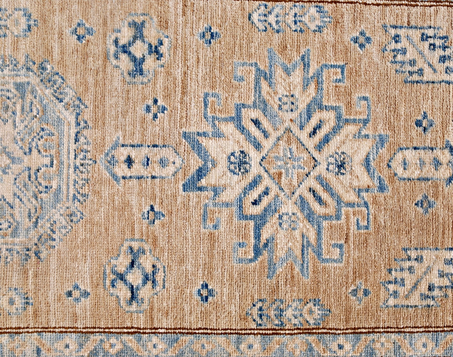 A handmade Afghan Super Kazakh runner featuring traditional blue geometric motifs on a tan wool base.