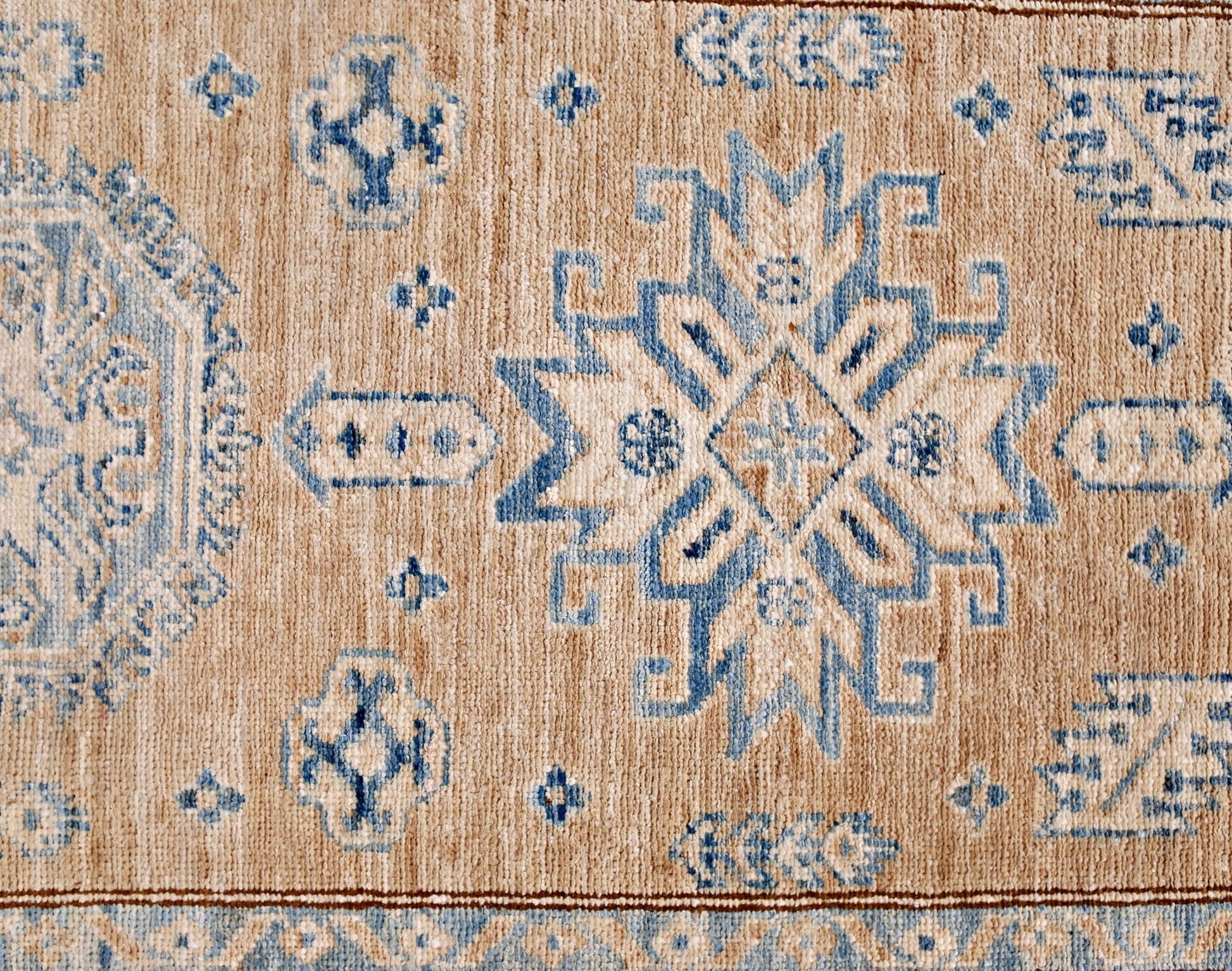 A handmade Afghan Super Kazakh runner featuring traditional blue geometric motifs on a tan wool base.